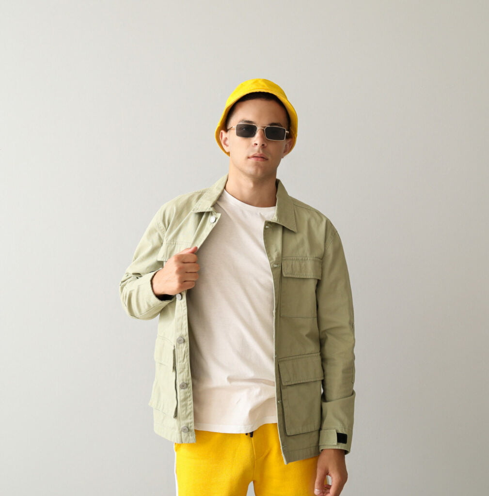 Young man in stylish bucket hat and jacket on light background